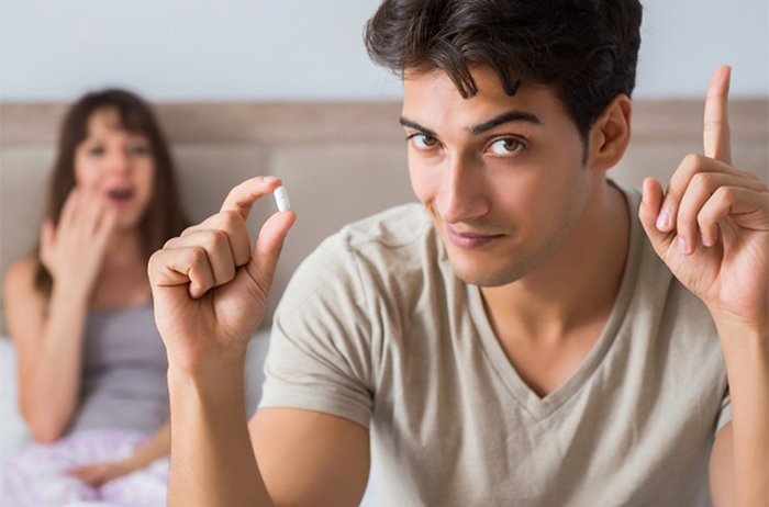 Young man in bed with wife about to take a Herbal Mojo for Guys instant erection pill