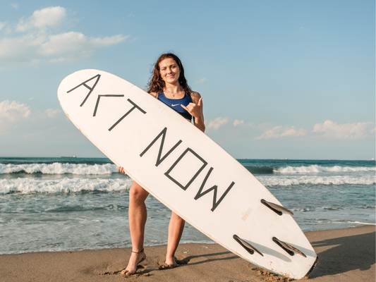 Surfer with Act Now printed onto the underbelly of her surfboard