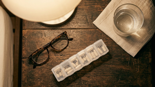 Overhead view of a pill organizer and glass of water on a nightstand, representing medication interactions to consider before taking Herbal Mojo