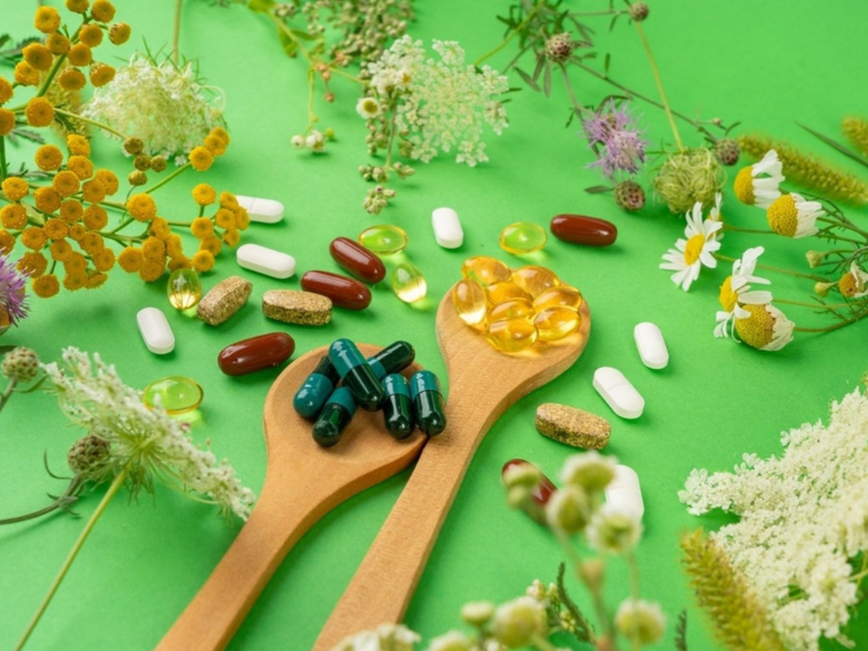 Natural herbal supplements and capsules alongside prescription pills, surrounded by medicinal flowers and herbs