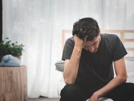 Man sitting on a bed looking concerned about erectile dysfunction and “instant pill” claims