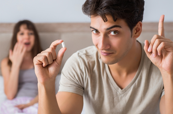 Young man in bed with wife about to take an Erectimus instant erection pill