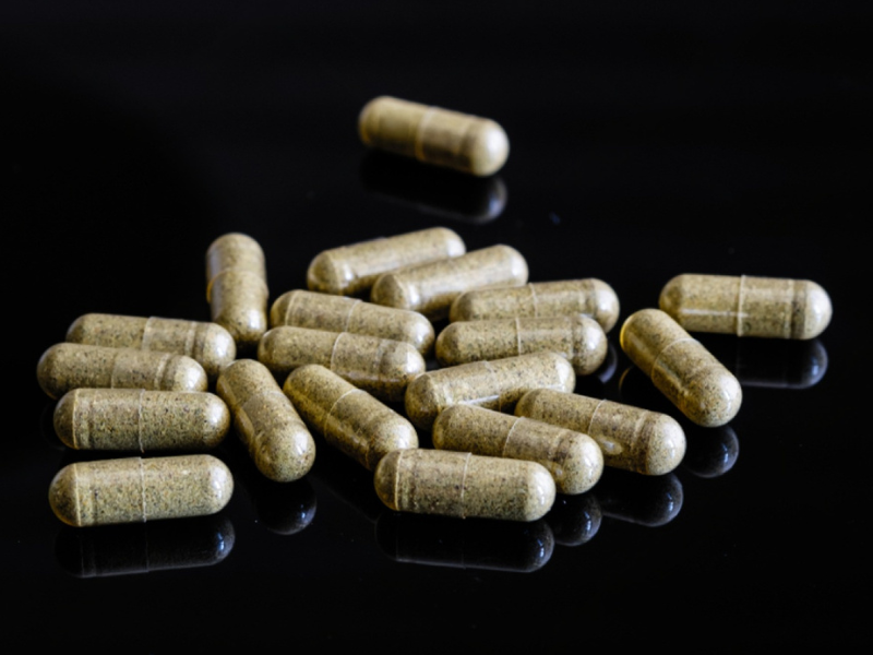 Herbal supplement capsules on a reflective black surface
