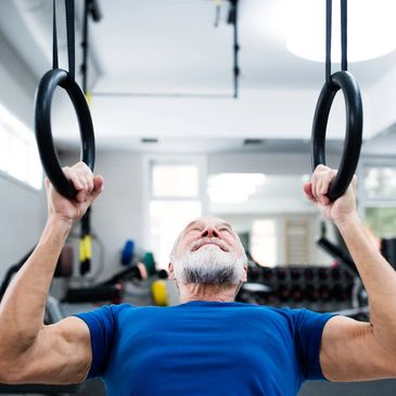 Older man exercising on gymnastic rings in a gym