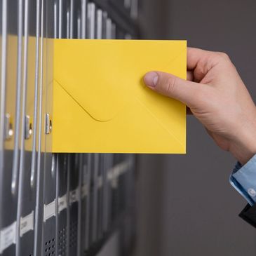 Hand placing a yellow envelope into a metal mailbox slot