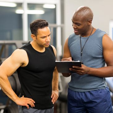 Two men in a gym one taking notes while the other looks on